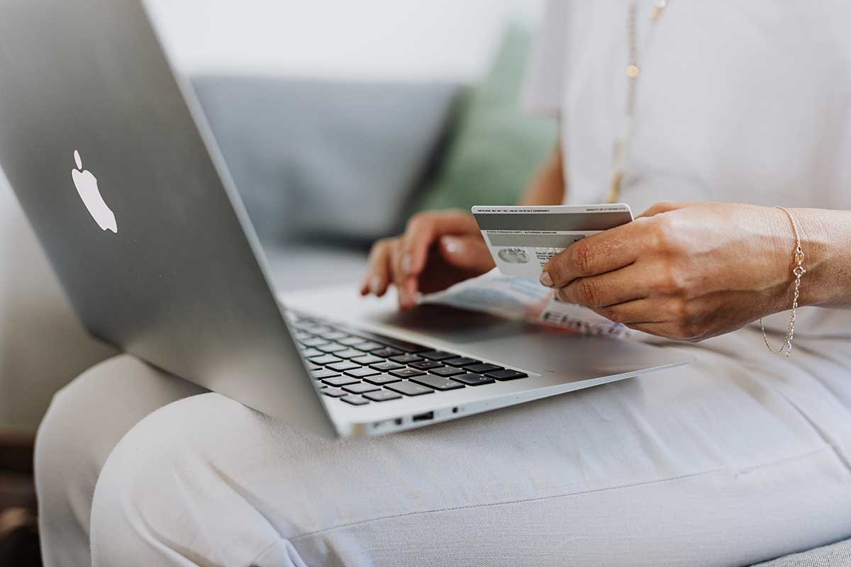 Mulher a usar um macbook e a segurar um cartão de crédito